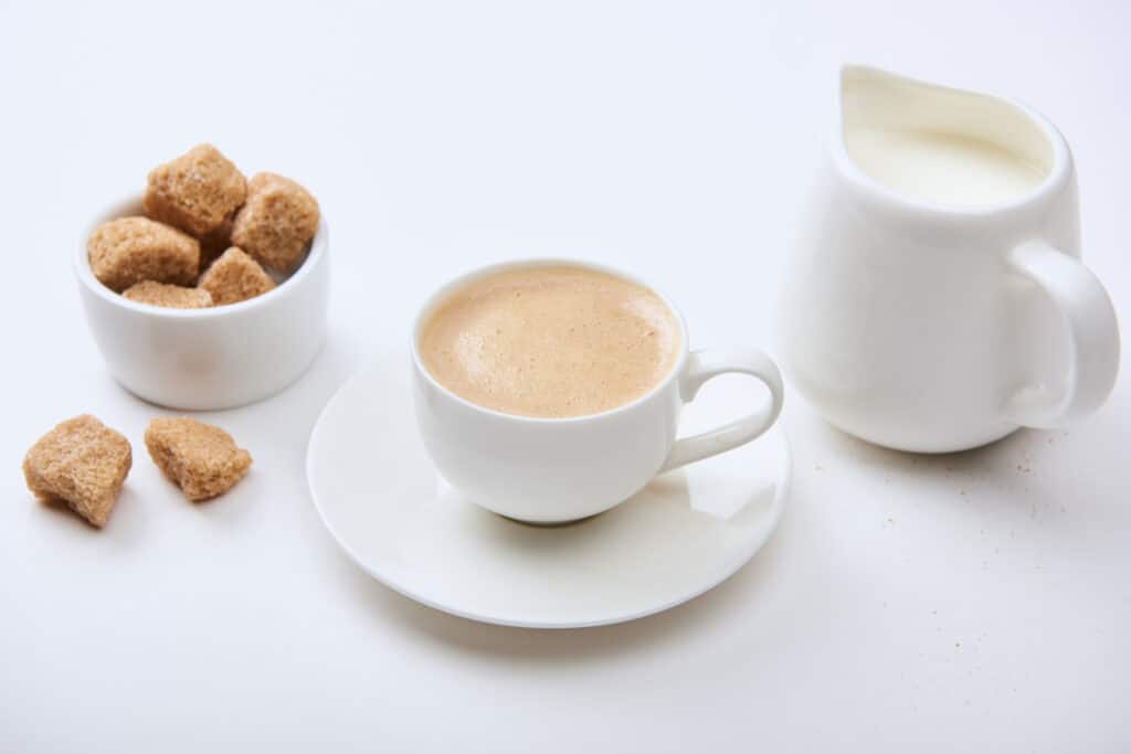Café con leche y azúcar, servido en porcelana blanca.