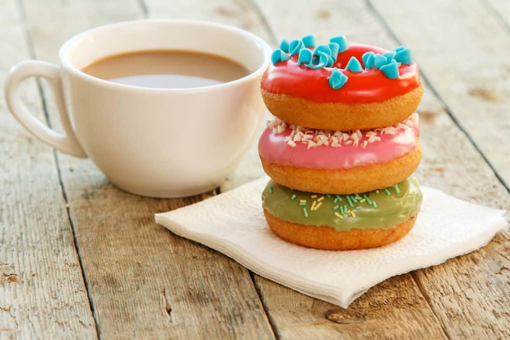 Coffee cup next to three sugar glazed donuts